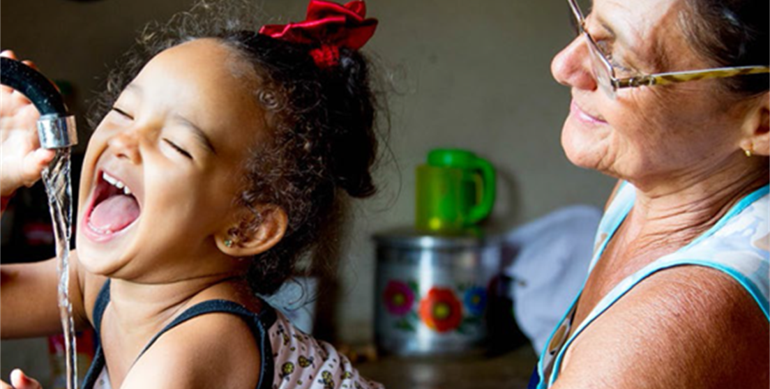Niña bebiendo agua de un grifo